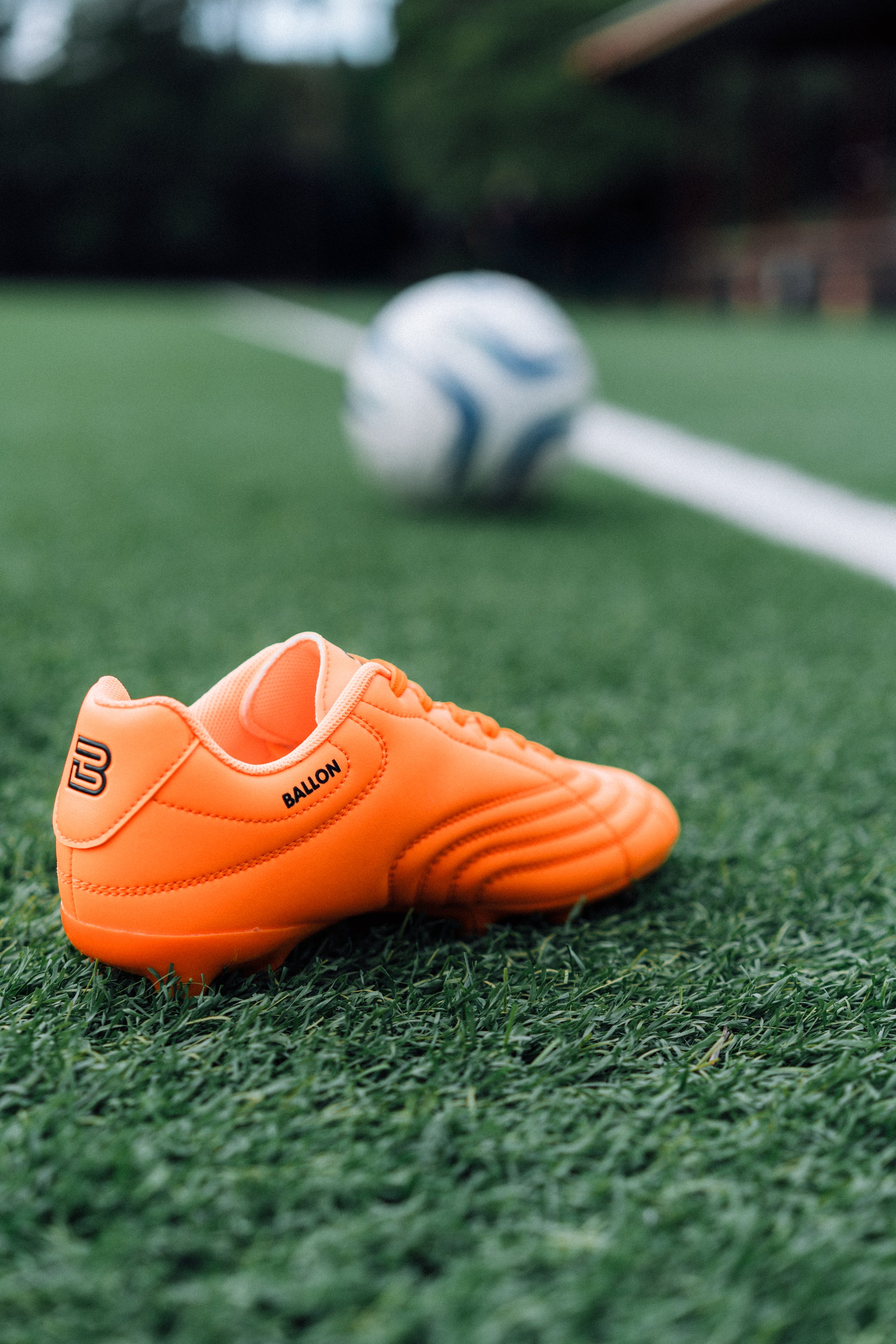Orange soccer cleat on a grass field with a blurred soccer ball in the background