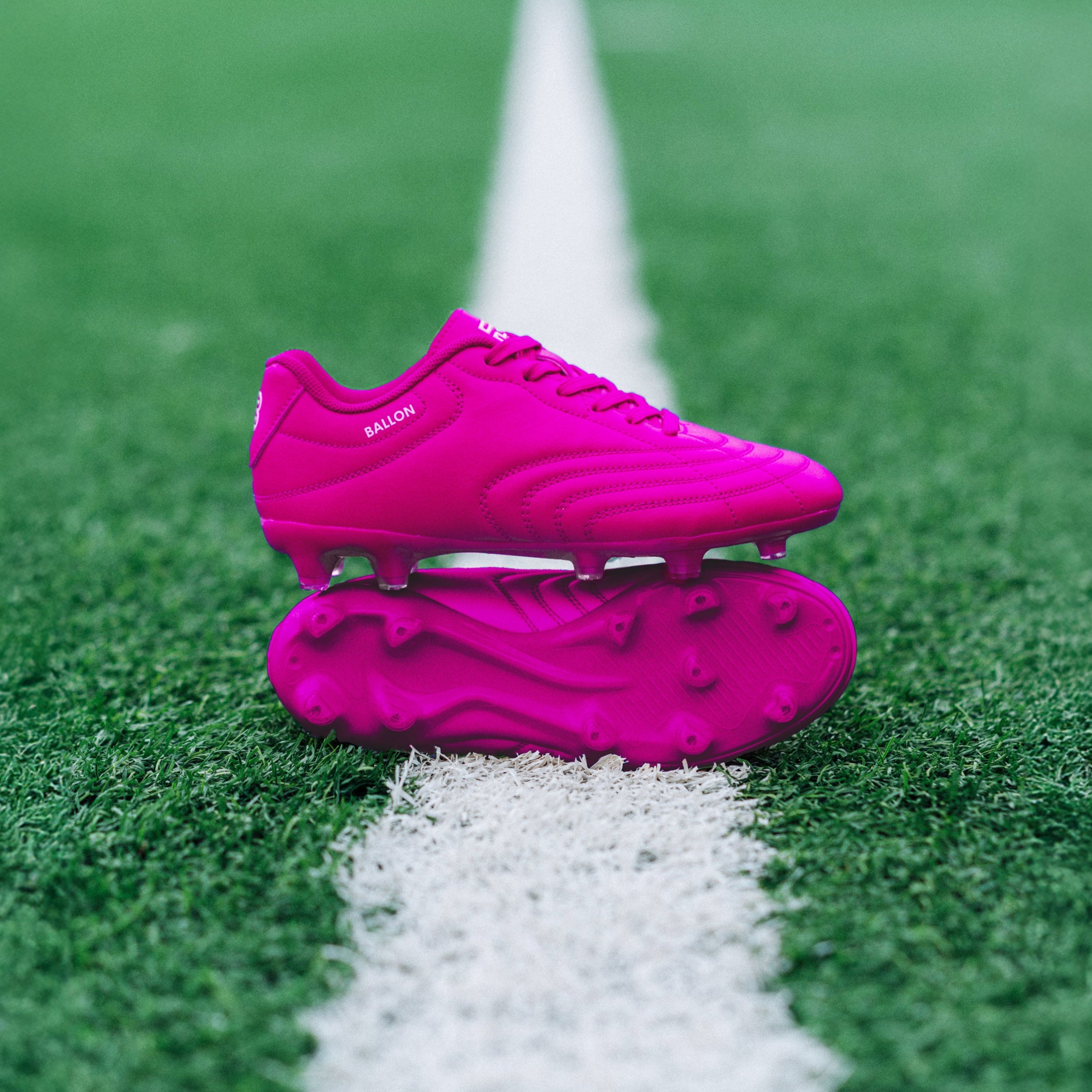 Pink soccer cleat on a green field with a white line