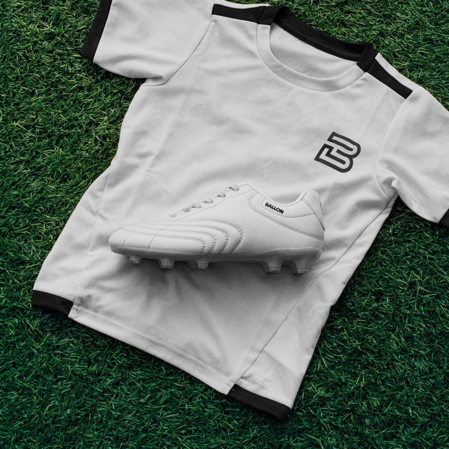 White sports jersey with black trim and a logo, paired with a white cleat on grass.